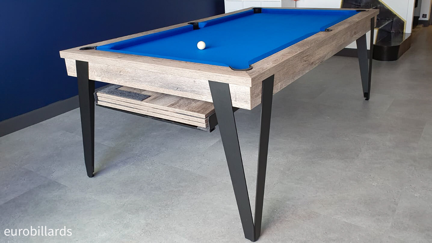 Cette table de style industriel —finition chêne oldtimer sur quatre pieds en métal fin noir pliés— se transforme en billard américain au tissu bleu par la simple dépose des 3 éléments de plateaux qui se dissimulent dans la nacelle pendant le jeu.